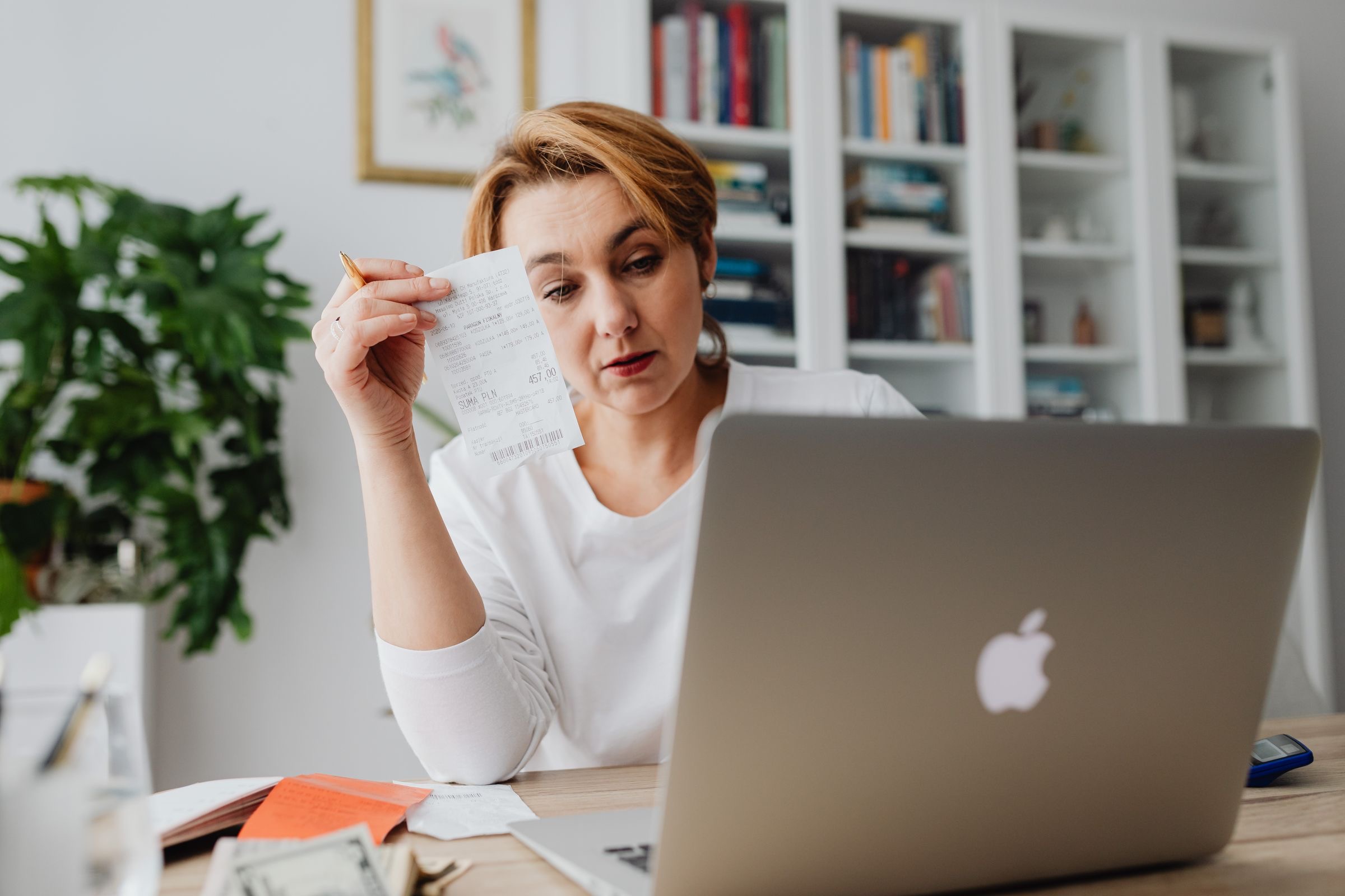 A founder at a small desk sorting receipts next to a laptop with a spreadsheet