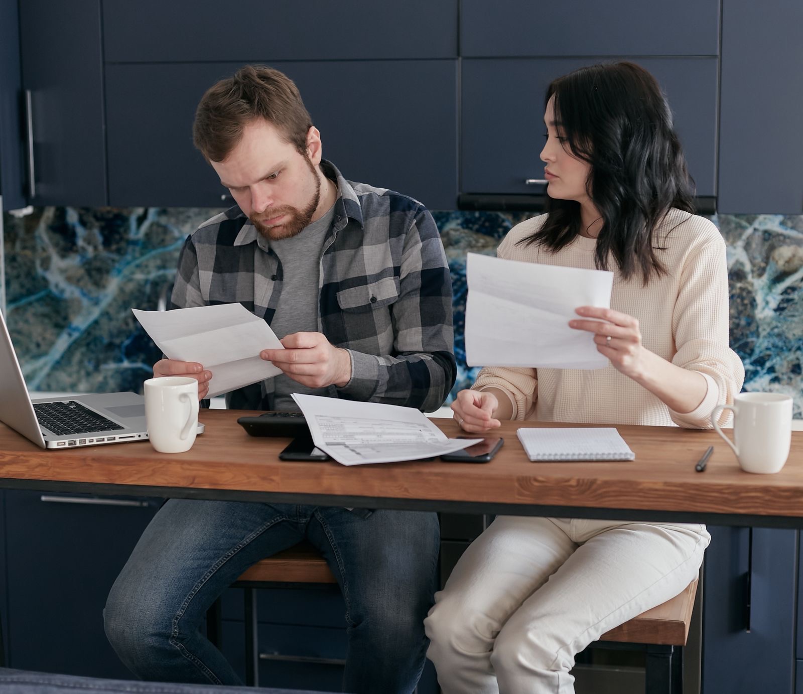 Two people at a table reading printed documents beside a laptop