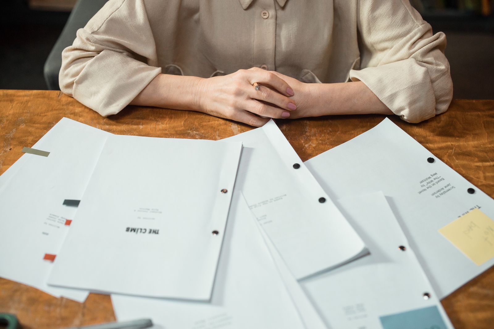 Hands sorting printed contracts into a folder beside a laptop on a desk