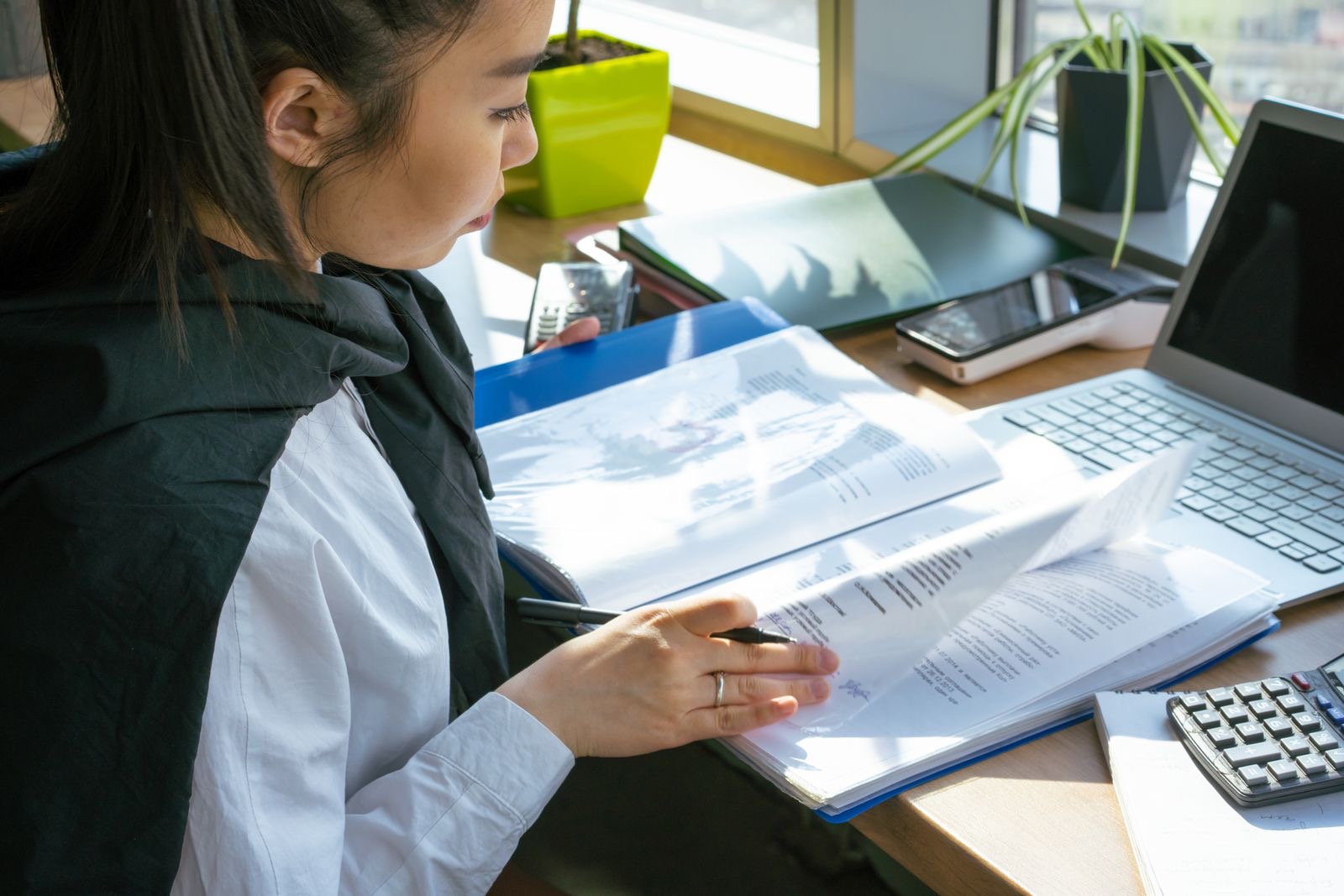 A laptop and documents on a desk by a window in daylight