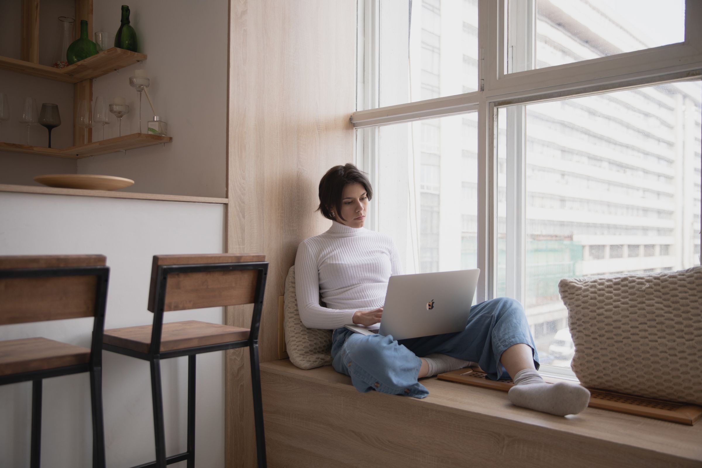 A young founder working on a laptop on a window seat at home