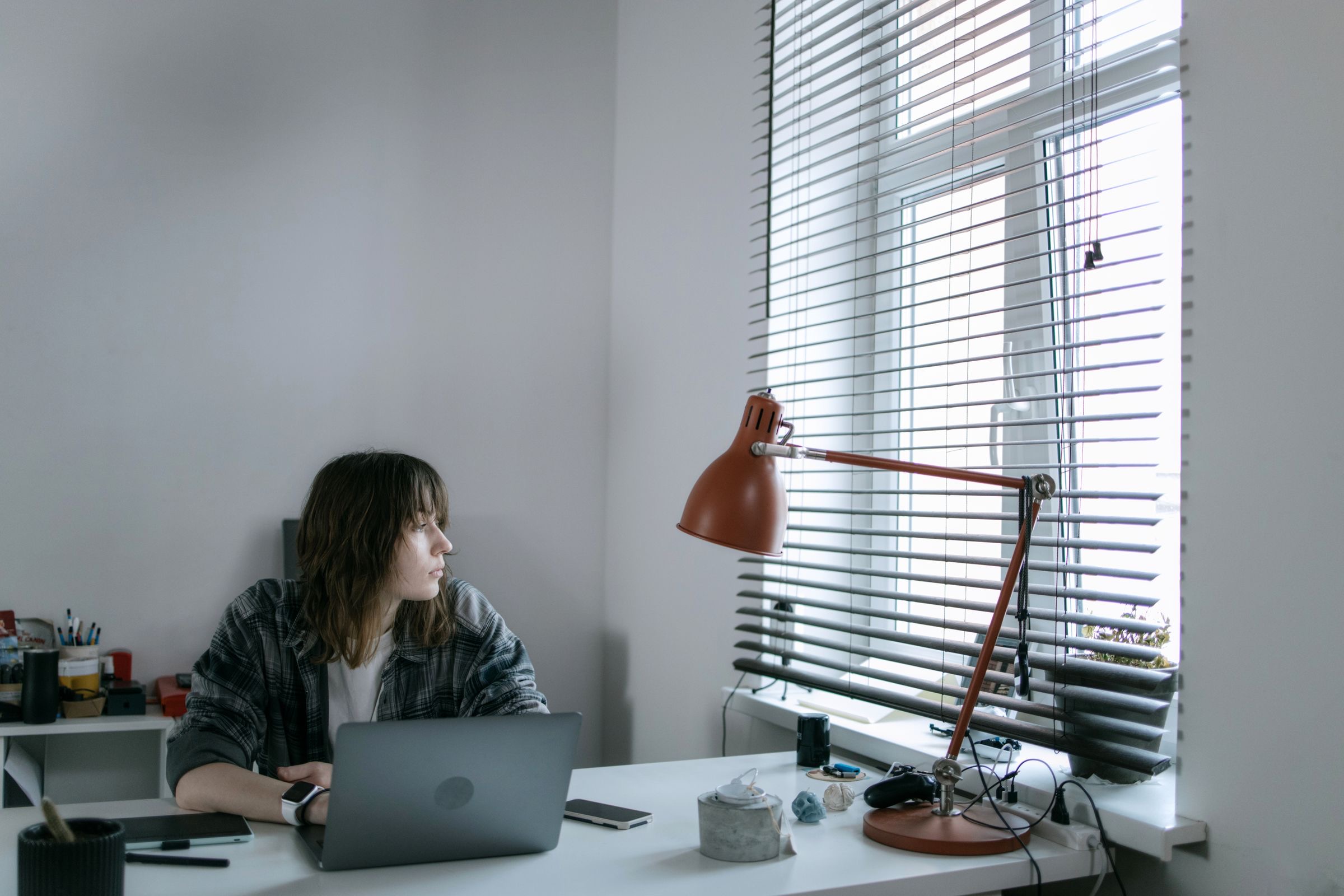 A freelancer at a laptop with a few papers on a table by a tall window in daylight