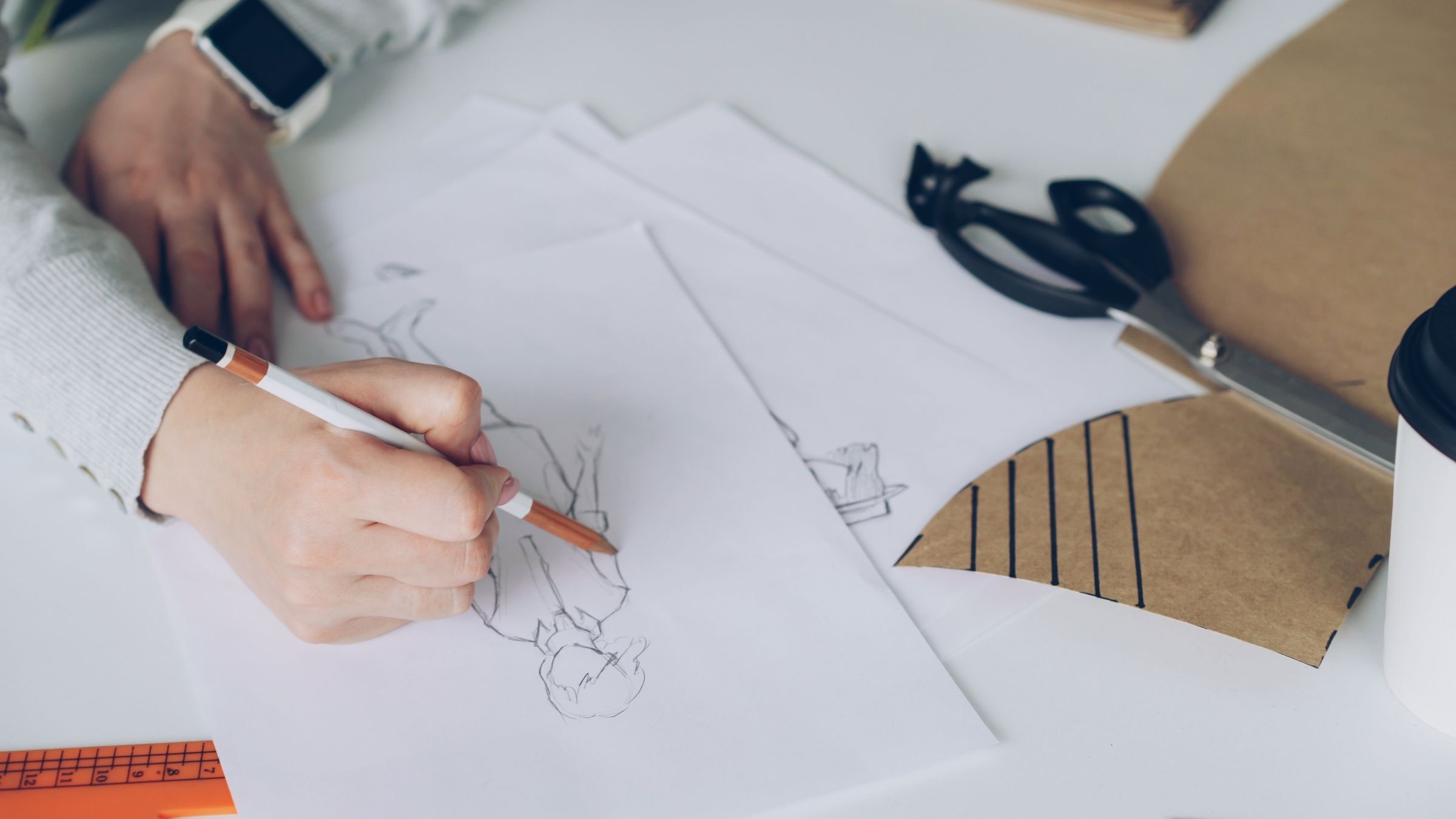A hand sketching drafts on paper at a desk